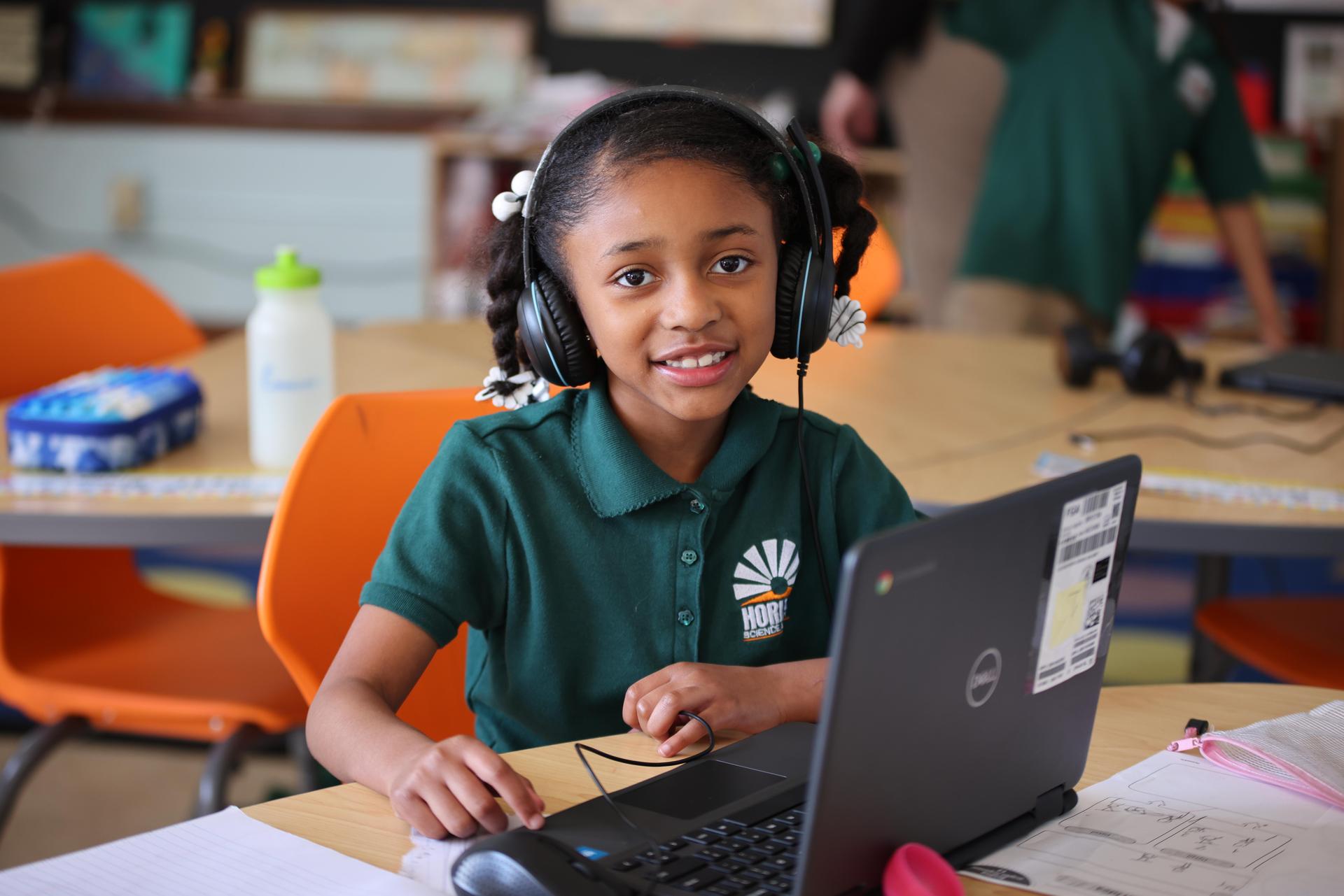 Student wearing headphones and working on a laptop in a classroom.