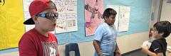 Three children interacting in a classroom environment with learning materials and water bottles.