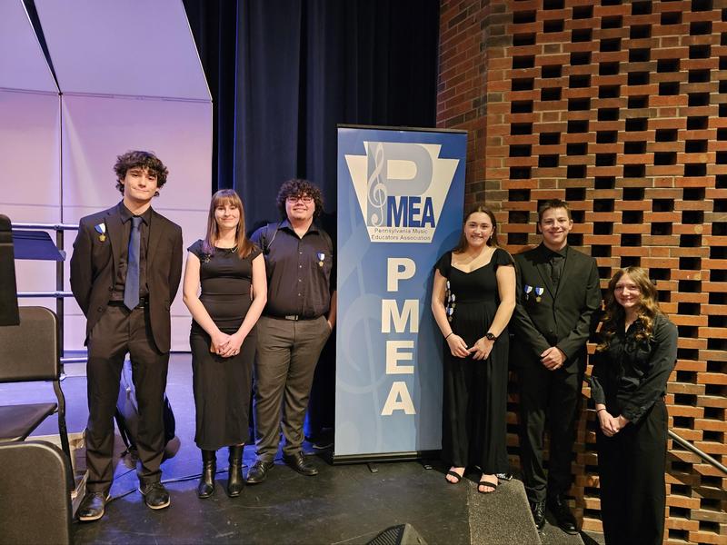 students dressed in black stand on stage around PMEA sign