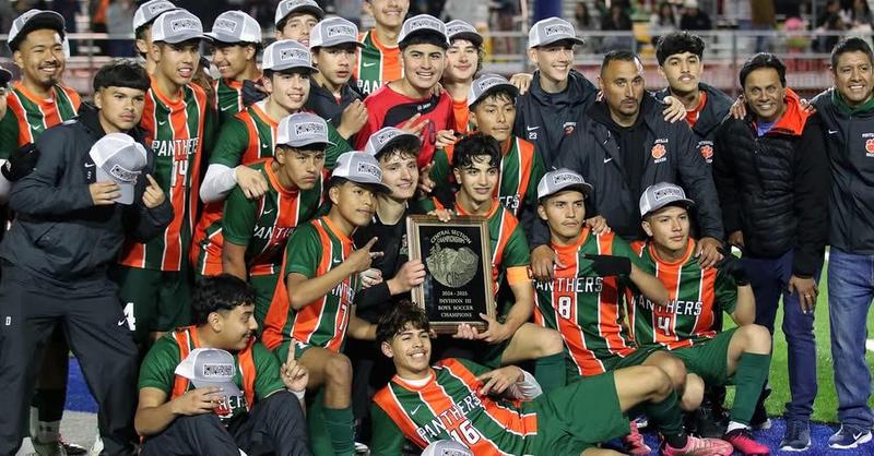 A large group of high school soccer players from Porterville High School, dressed in green and orange striped uniforms with 'Panthers' on the front, celebrate their Central Section Division III championship victory. The team proudly holds a championship plaque while wearing matching gray 'CHAMPIONS' hats, surrounded by coaches and staff, all smiling on a turf field under stadium lights.