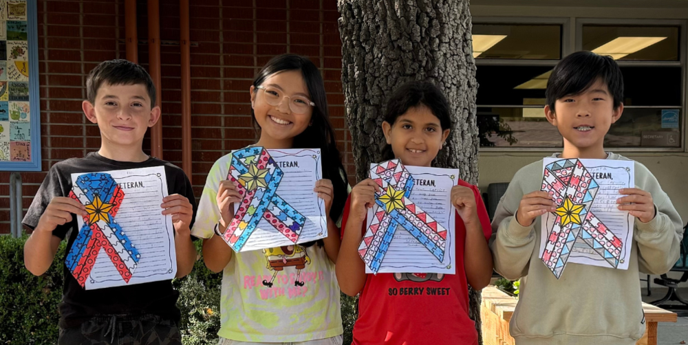 Four children proudly holding decorated papers with ribbons outside.
