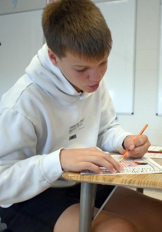 A boy focused on coloring a worksheet while sitting at a desk.