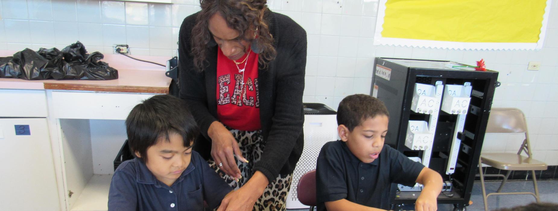 A teacher assists two students with a crafting activity at a table.