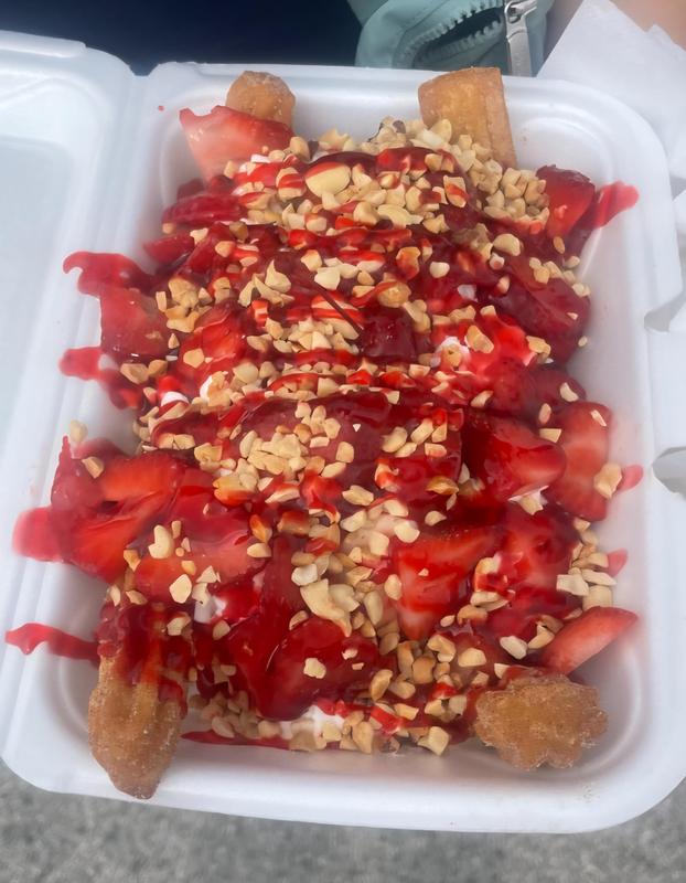 Churros topped with strawberries, chocolate syrup, and crushed peanuts in a container.