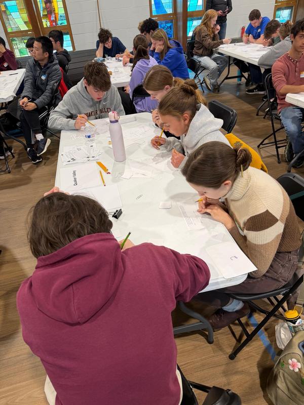 Candid photo of five QVHS students are sitting around a table where they are working on math problems.