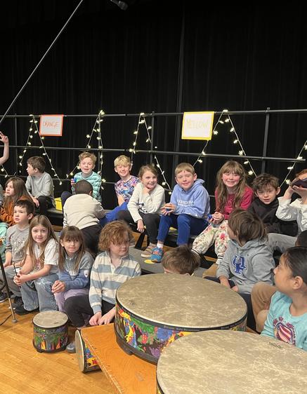 Children seated with drums, smiling and enjoying their performance.