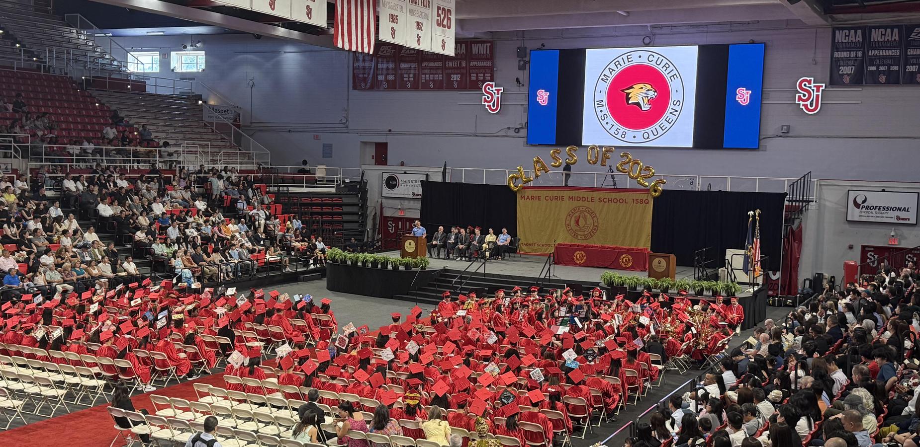 Graduation ceremony with students in red caps and gowns seated in rows.