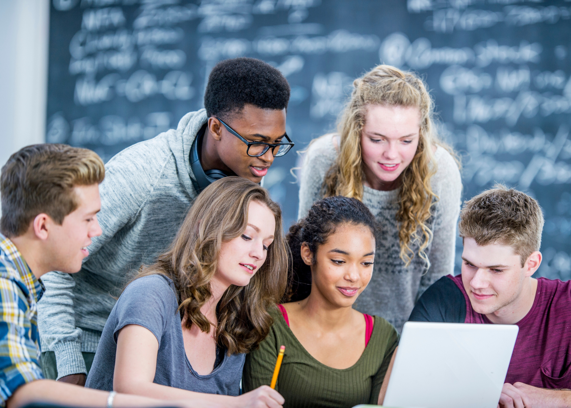 A group of high school aged students crowded around a computer