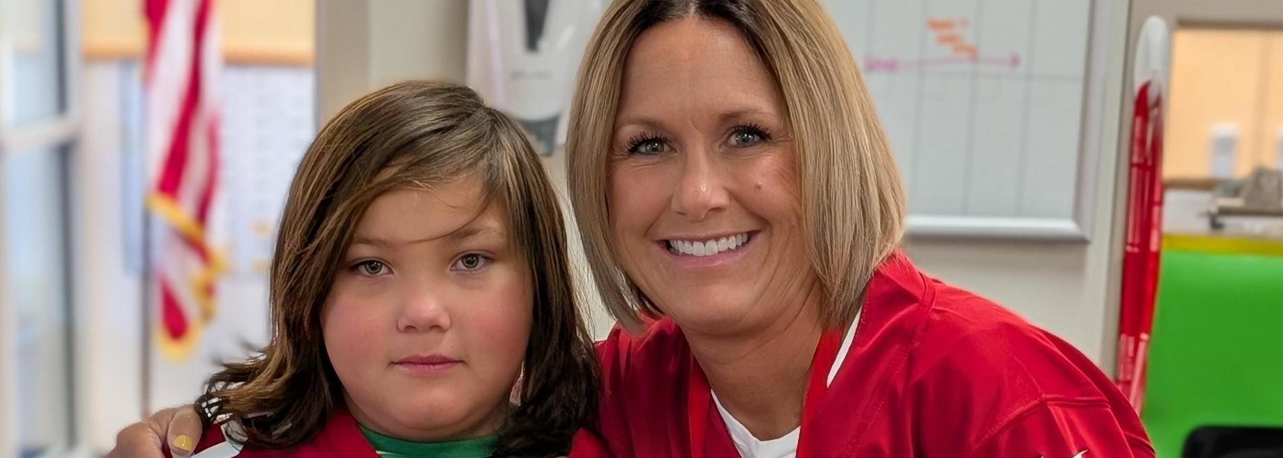 A smiling woman and child pose together in a classroom setting.