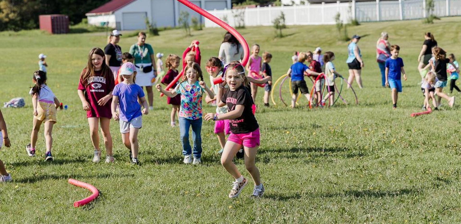 Children playing outdoors on a grassy field with colorful jump ropes.
