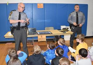 Two police officers speaking to a group of children in a gymnasium.