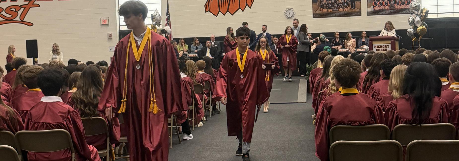Students in maroon graduation gowns walking during a ceremony.