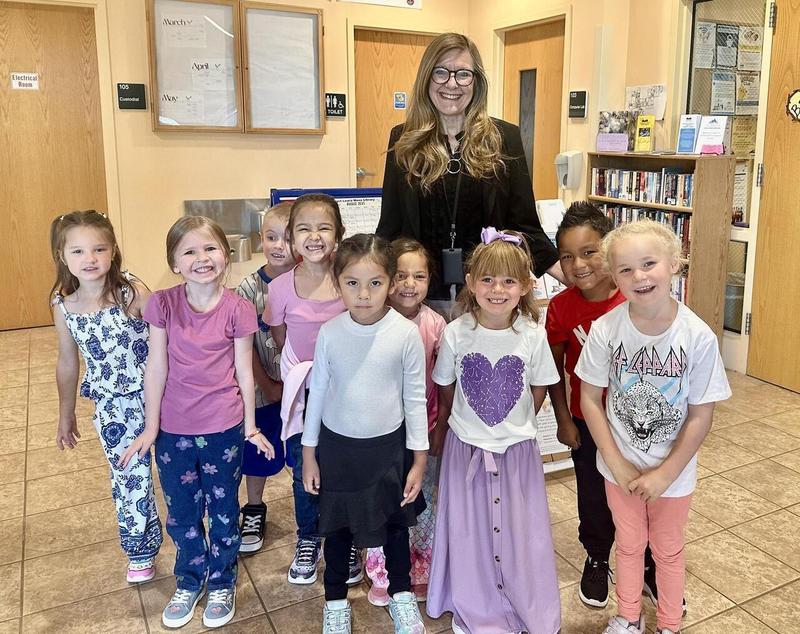 A smiling adult stands with a group of happy children in a school foyer