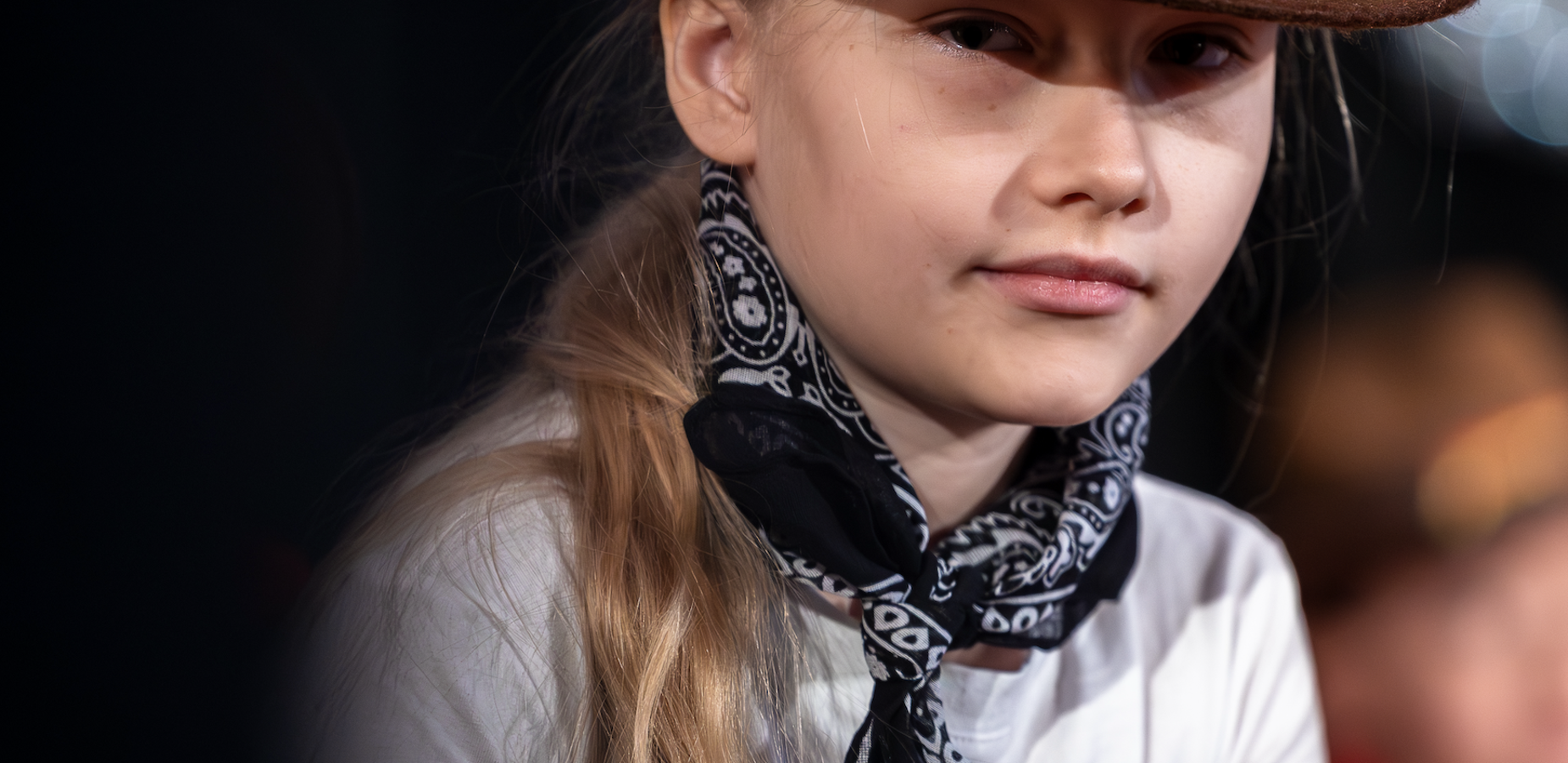 Girl with long hair wearing a cowgirl hat and a black bandana.