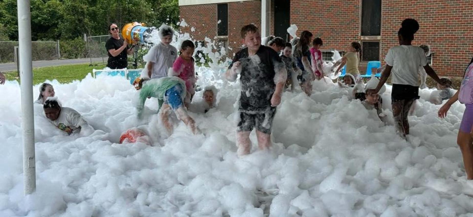 Children playing in a field filled with foam, enjoying a fun outdoor event.