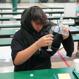 A boy pours water into a measuring cylinder
