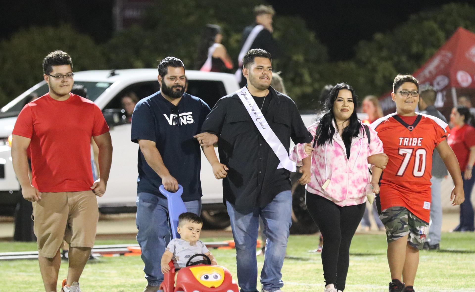 homecoming king and queen candidates walking across the field with their escorts
