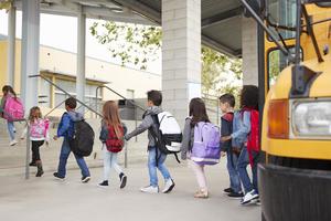 Students arriving at school, a bus has its doors open nearby.
