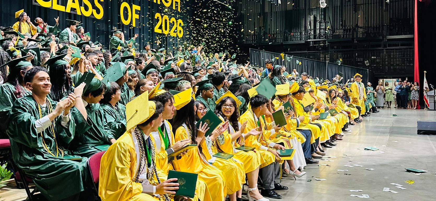 Graduating class in caps and gowns celebrating during a ceremony with confetti.