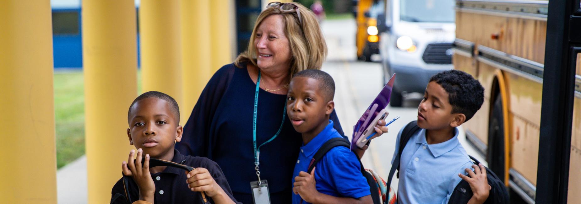 A teacher hugs students as they arrive for school