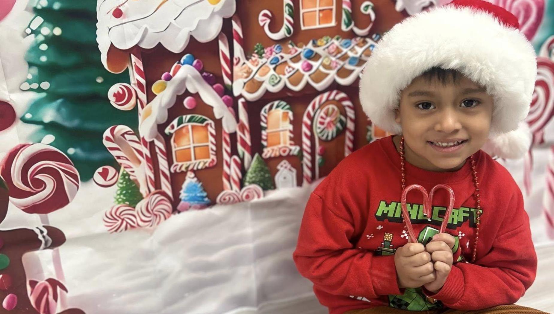 A boy in a Santa hat holding candy canes in front of a festive backdrop.