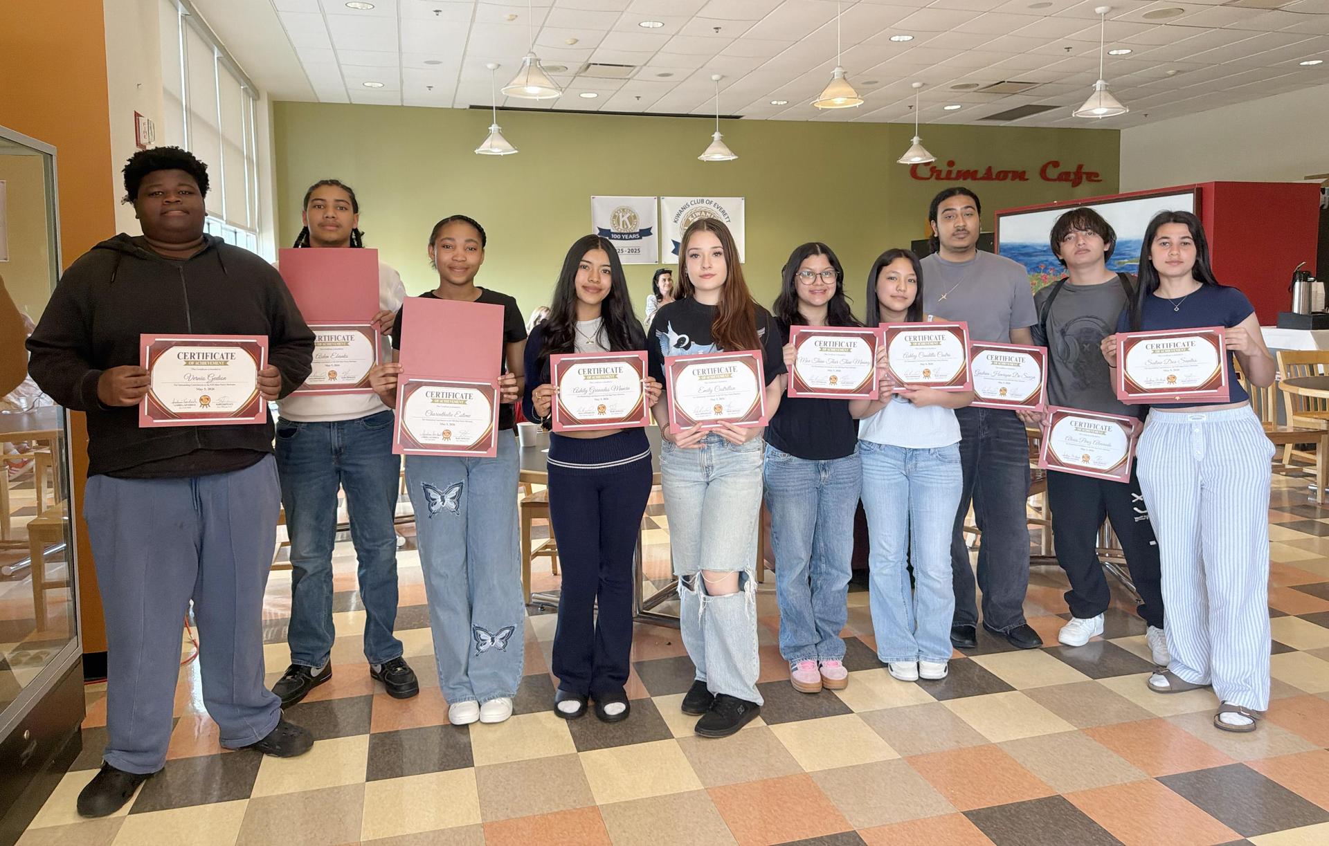 Students holding certificates in a cafe setting.