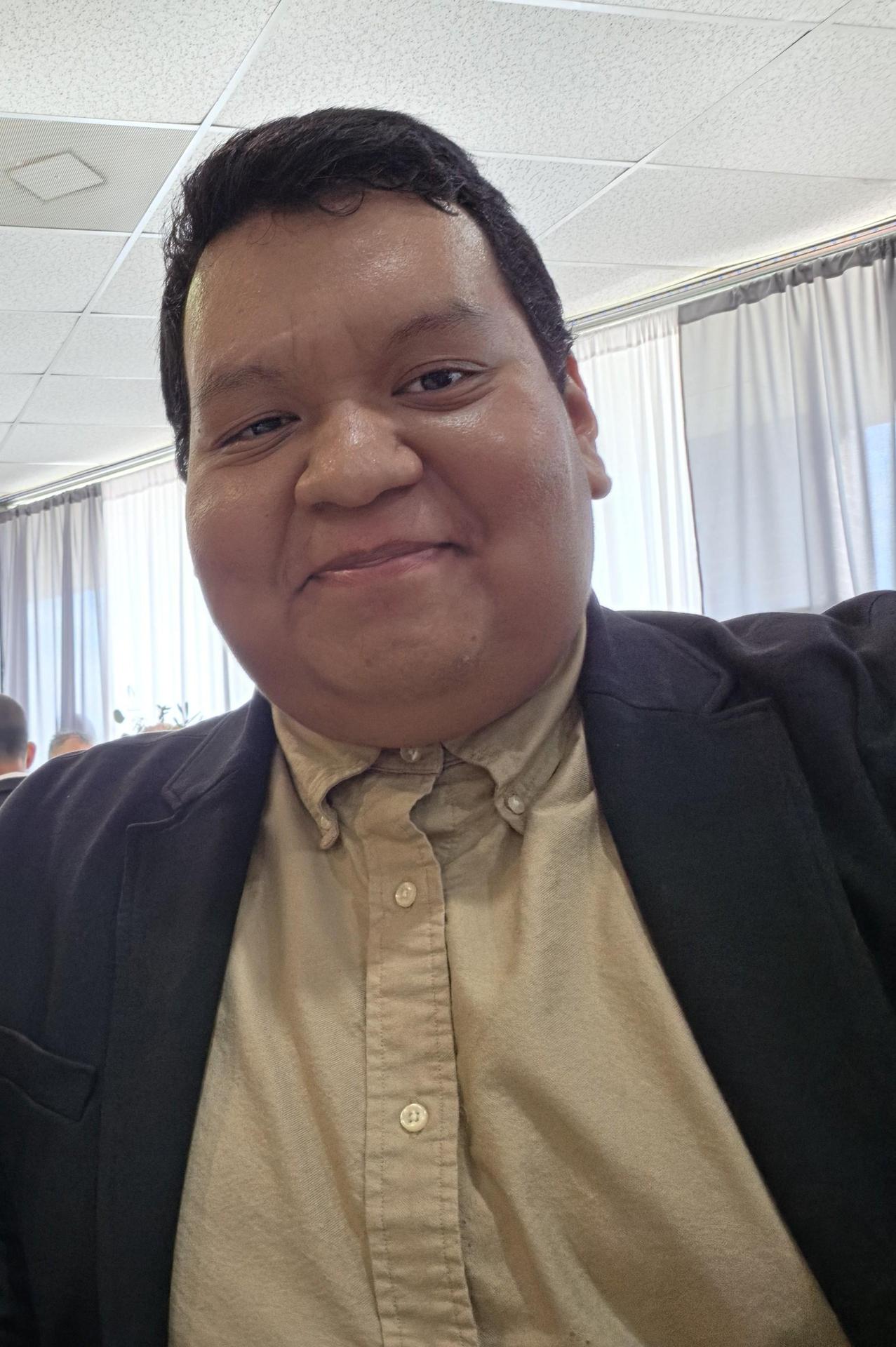 Person with short hair wearing a blazer, smiling in an indoor setting.