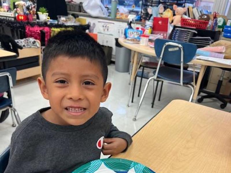 A boy beams while holding a decorated gingerbread cookie on a plate.