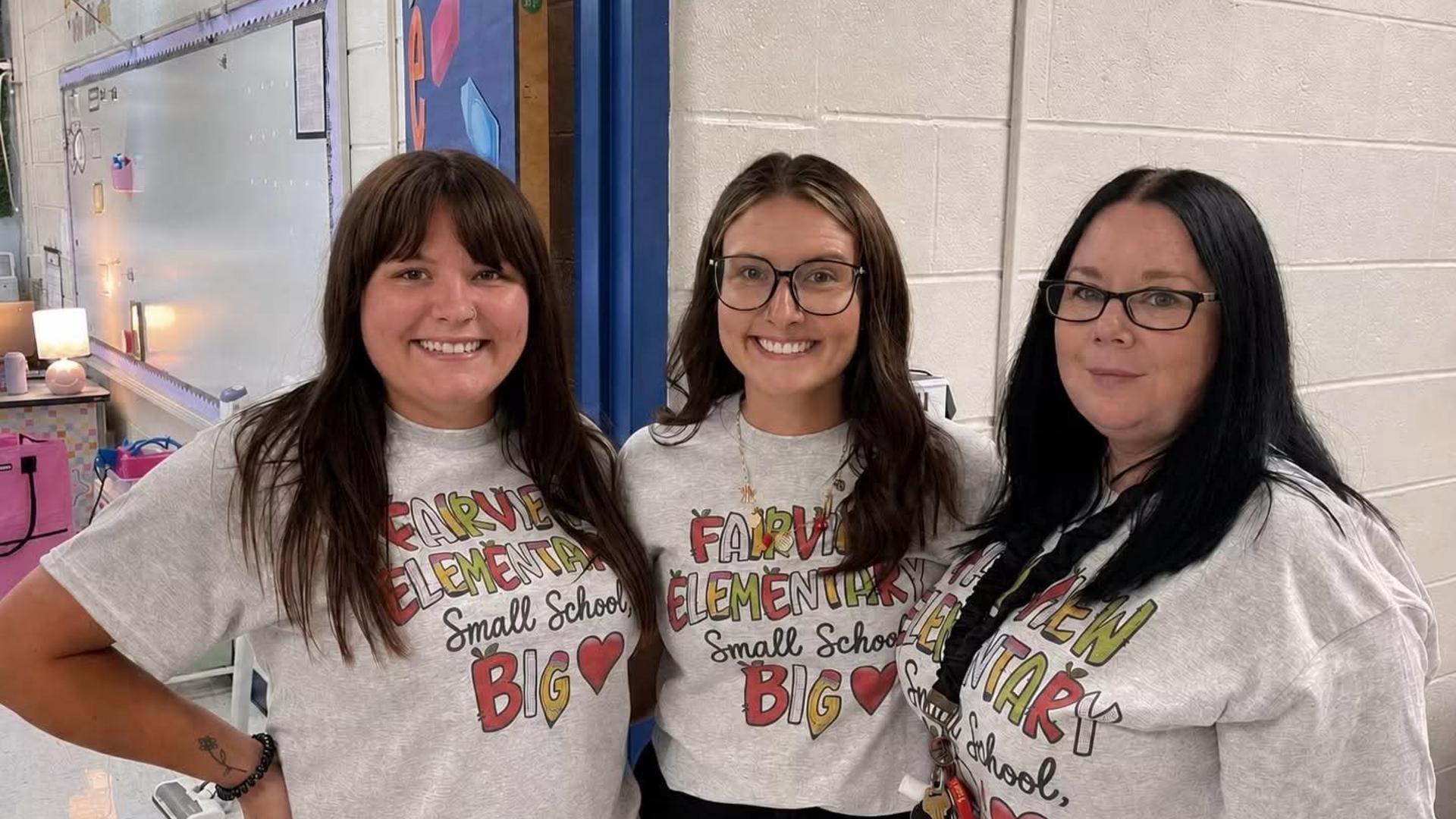 Three women wearing matching t-shirts stand together in a school setting.