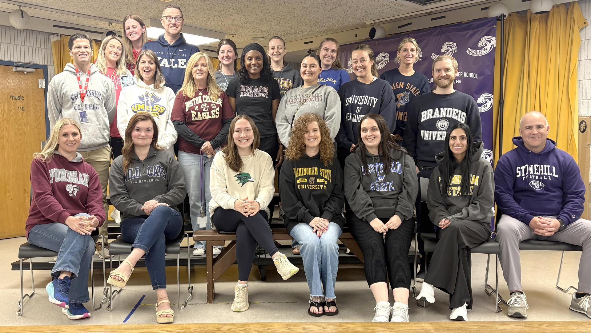 A diverse group of educators poses in university sweatshirts for a group photo.