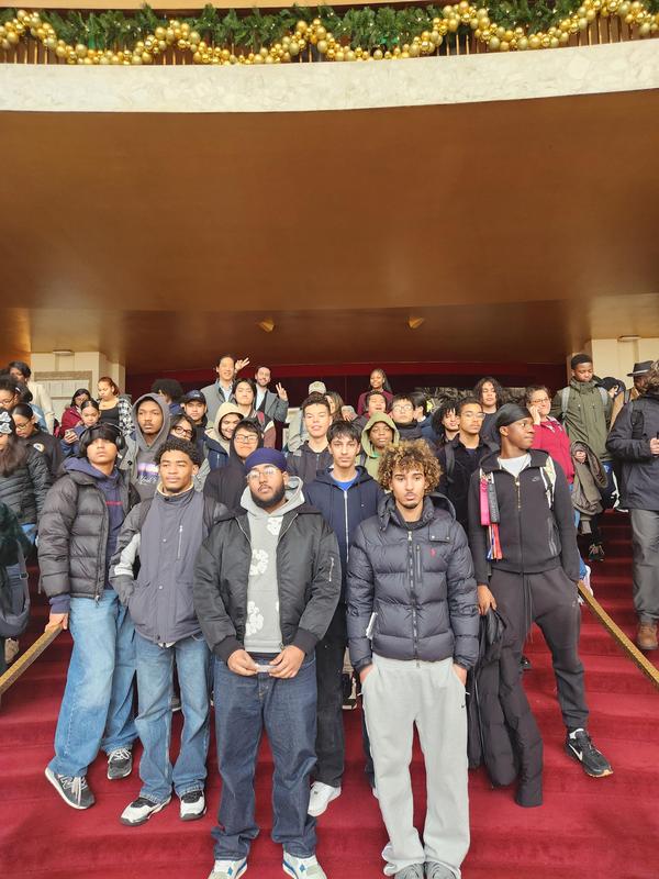 A group of students in winter clothing posing on the grand staircase of a theater.