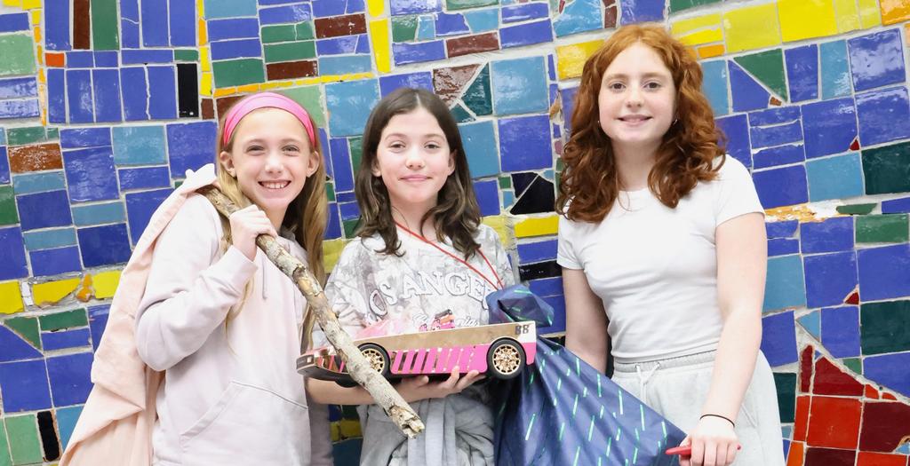 Three girls standing against a colorful tile wall.