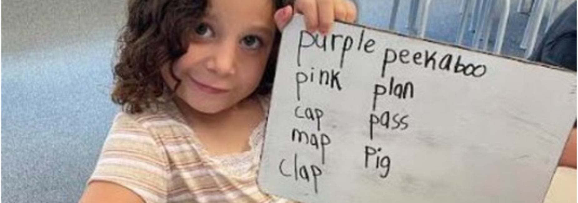 Child holding a whiteboard with listed words including colors and actions.