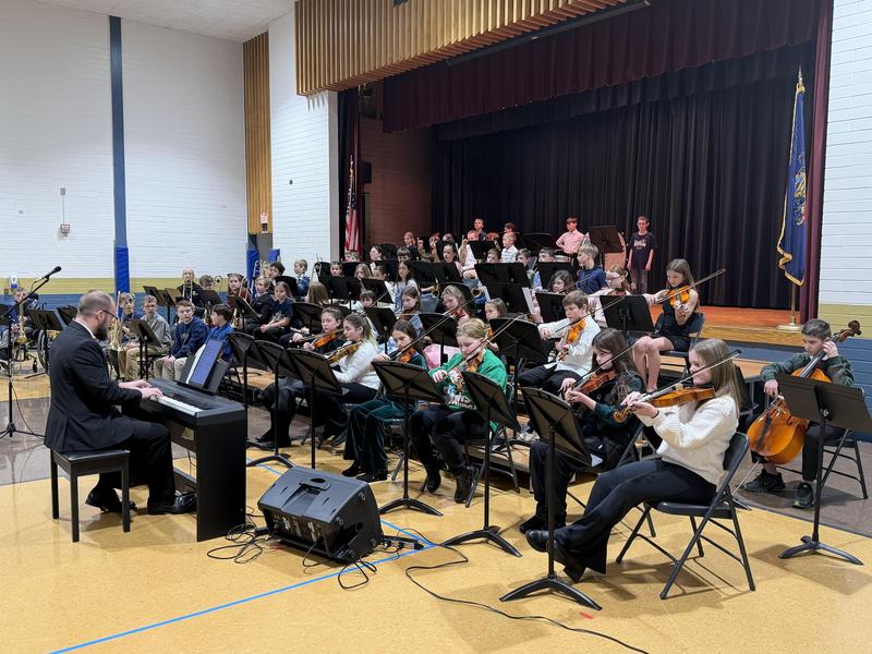large group of students holding band or orchestra instruments on stage
