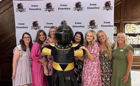 Group of people posing with a knight mascot at open house.
