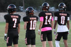 Four football players in black uniforms standing in a row, facing away.