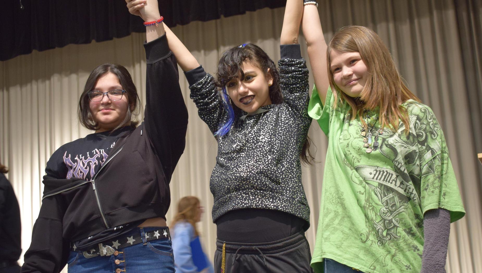 Three teenagers celebrating together with their arms raised.