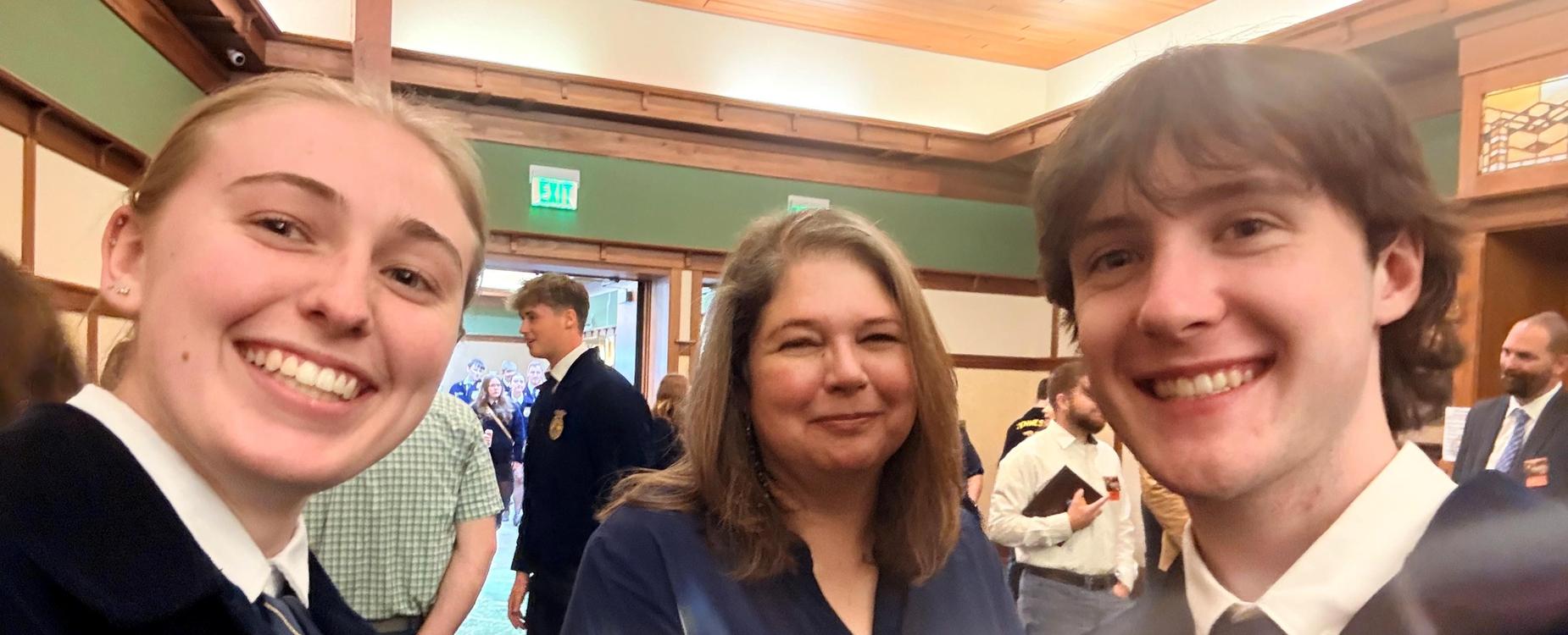 Three smiling individuals pose for a selfie at a gathering.