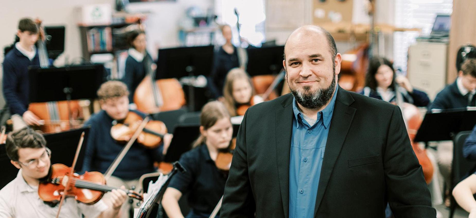 Orchestra teacher smiles in front of his student musicians