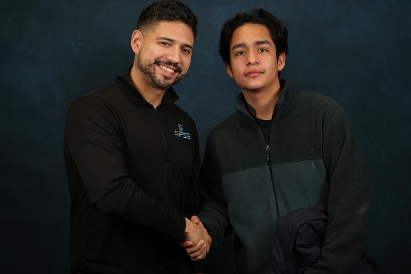 Two men smiling and shaking hands against a blue background.