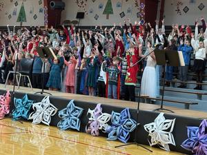 Children in festive attire cheer with raised hands during a concert.