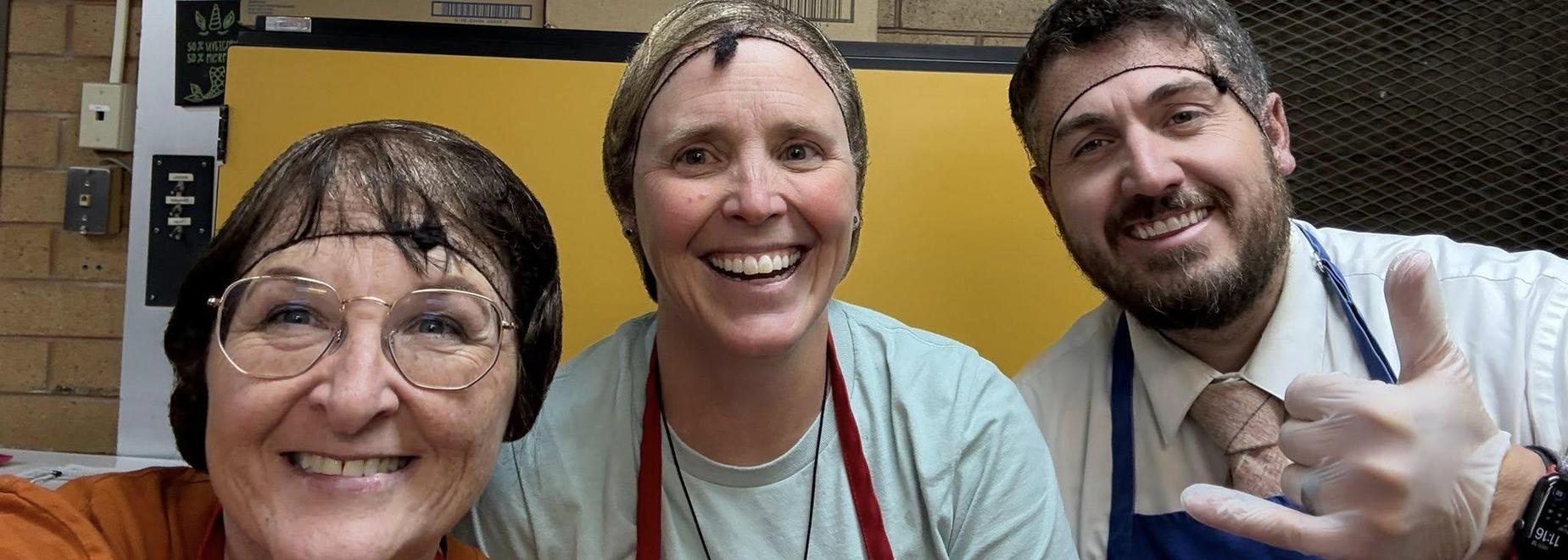 Three people smiling, wearing hairnets, in a casual indoor setting.