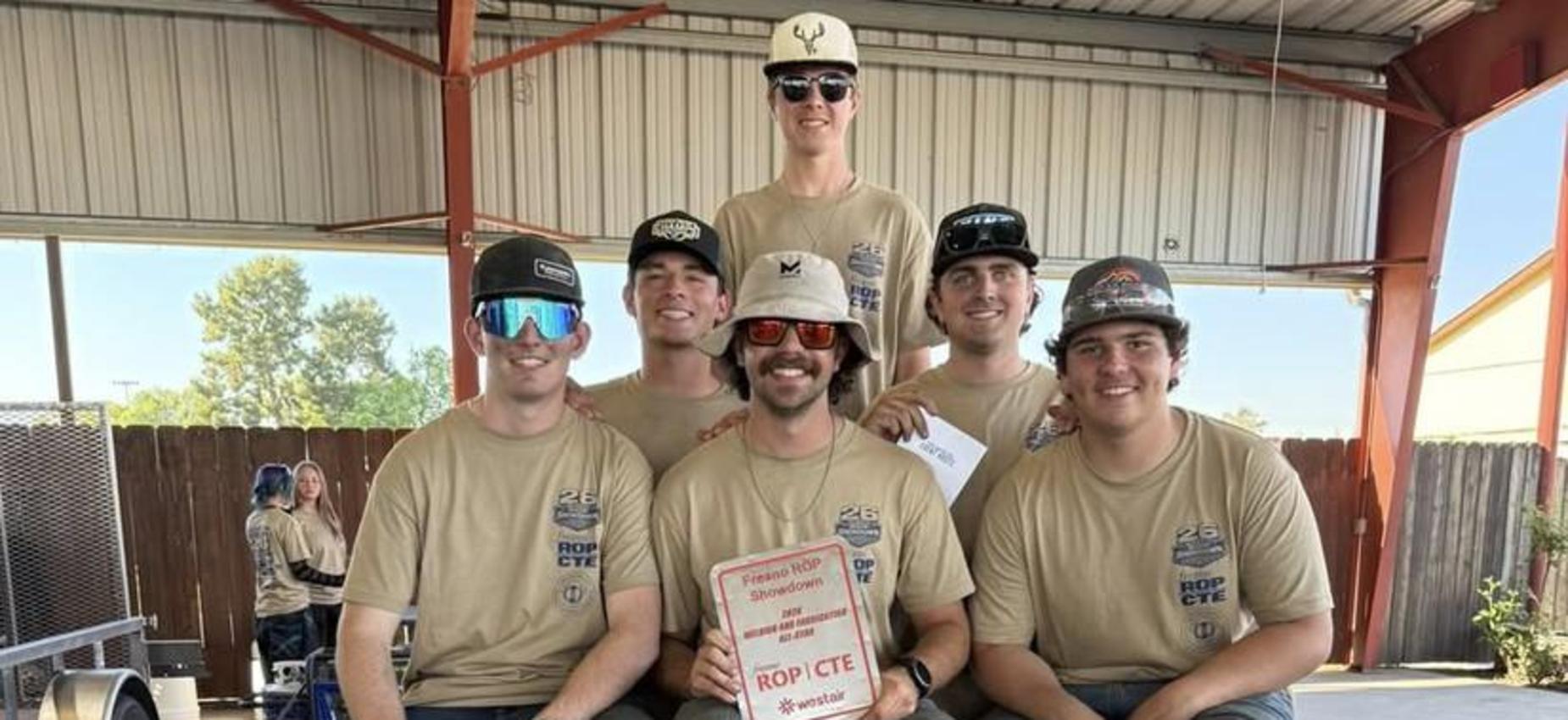 Three individuals sitting on a trailer holding an award in a workshop setting.