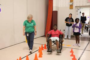 teacher standing by student who is navigating through orange cones in a wheelchair
