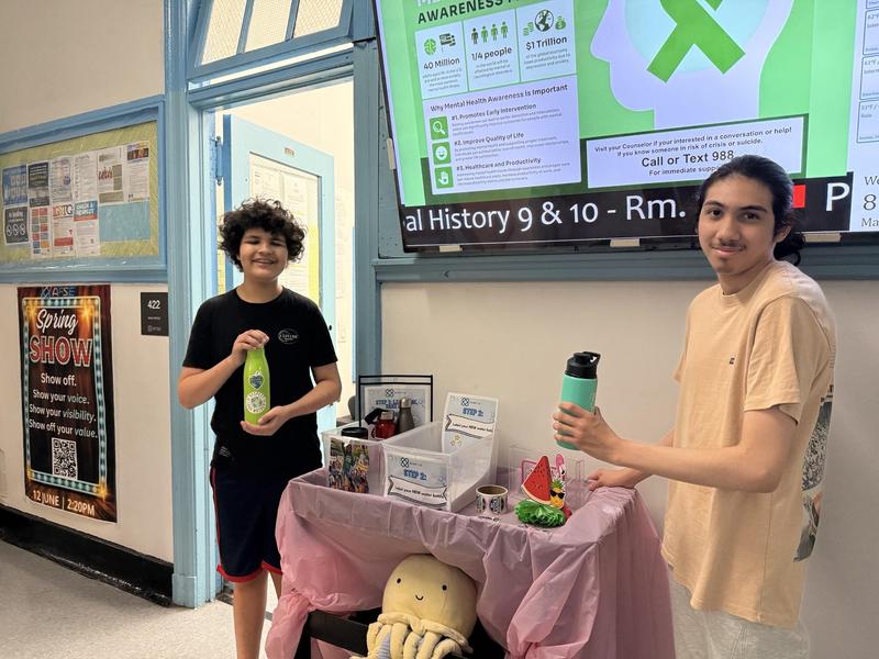 Two students holding water bottles in front of an information screen.