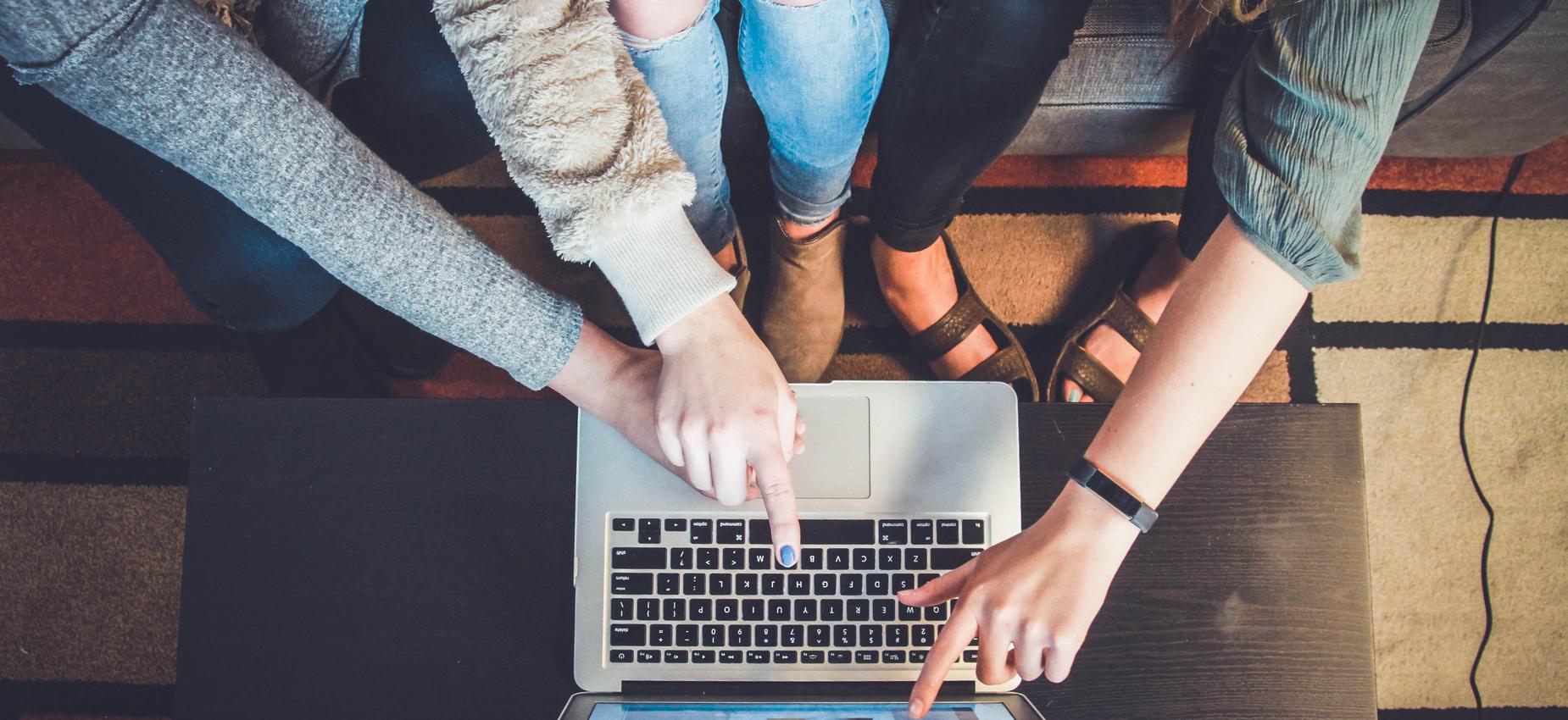 Three people pointing at a laptop during a collaborative work session.