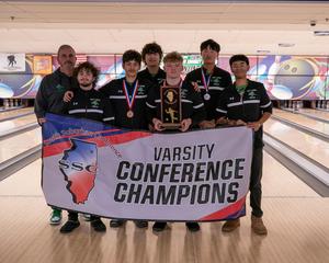 Bowling team holding a championship banner and trophy in a bowling alley.