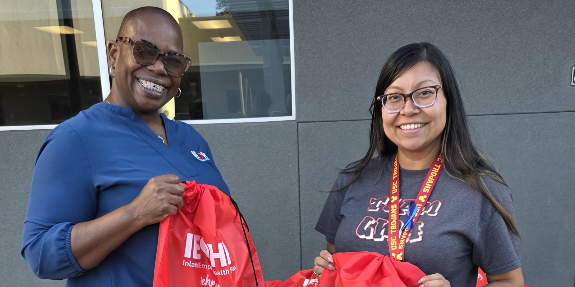 Two people holding red drawstring bags with logos, standing at a table.