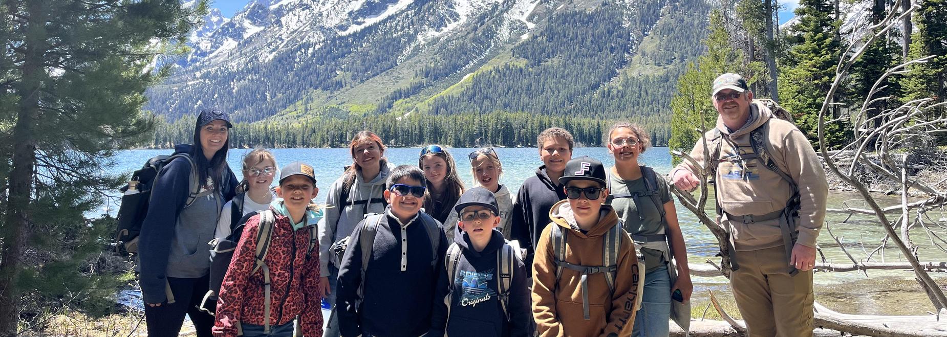 Group of people smiling near a lake with snowy mountains in the background.
