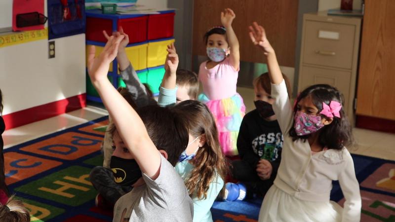 Photo of kindergartners raising their hands in class.